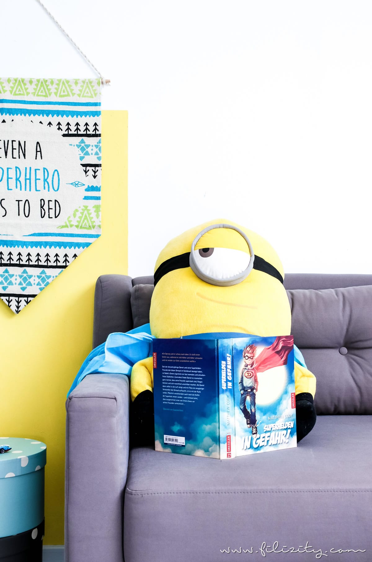 Wimpel aus buntem Teppich vor gelbem Hintergrund mit Minion auf der Couch | Kinderzimmer-Deko selber machen: DIY Wimpel aus Teppich | Filizity.com | DIY-Blog aus dem Rheinland #kinderzimmer #kinder #superhelden