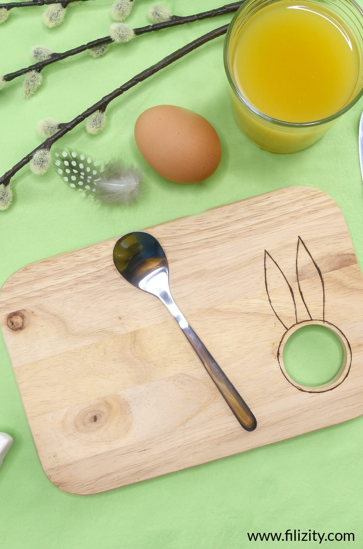 Selbst gemachtes Oster-Frühstücksbrett mit Eierbecher und Hasenohren Brandmalerei, ein Frühstücksei, ein Metalllöffel und ein Glas Orangensaft | Filizity.com - Kreativmagazin &DIY Blog